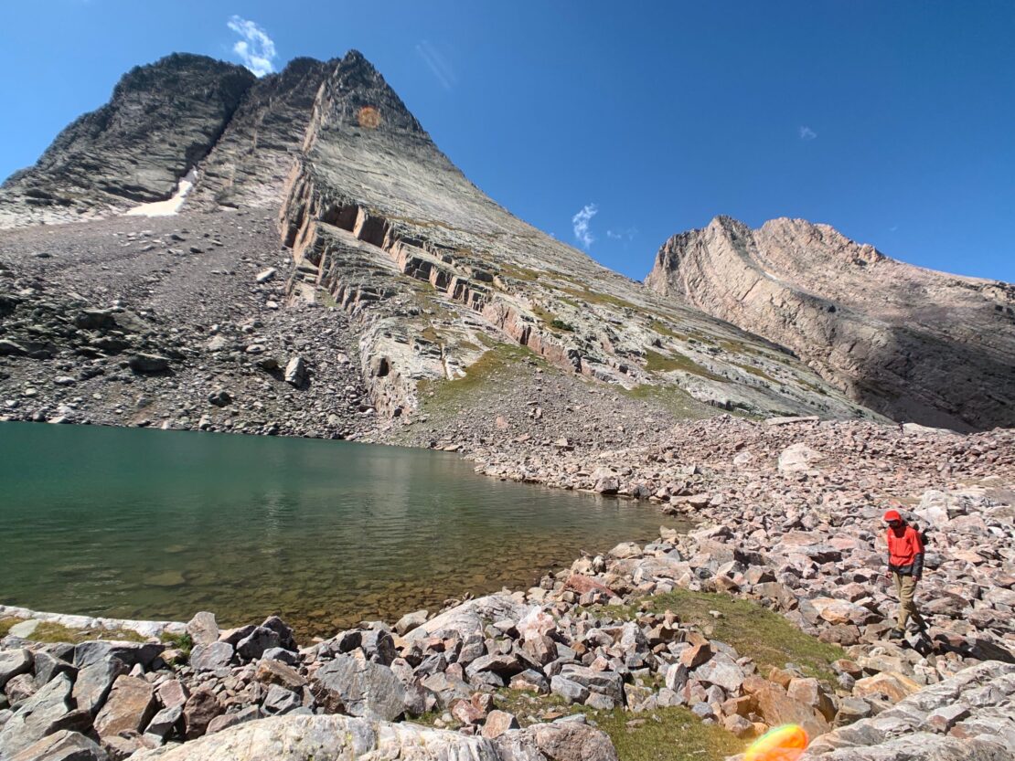 Client standing by an alpine lake at the base of Vestal Peak with blue skies