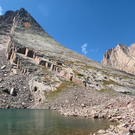 Climbers at the base of Vestal Peak with an alpine lake in the foreground.