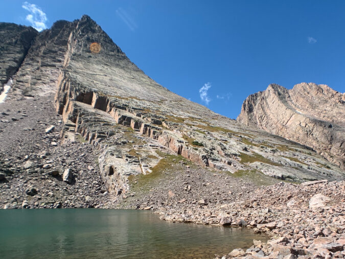 Climbers at the base of Vestal Peak with an alpine lake in the foreground.